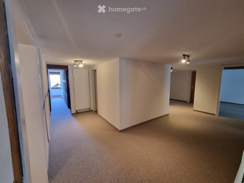 Empty hallway with beige carpeting, white walls, and recessed lighting. Doors lead to other rooms, including a balcony area visible at the end.