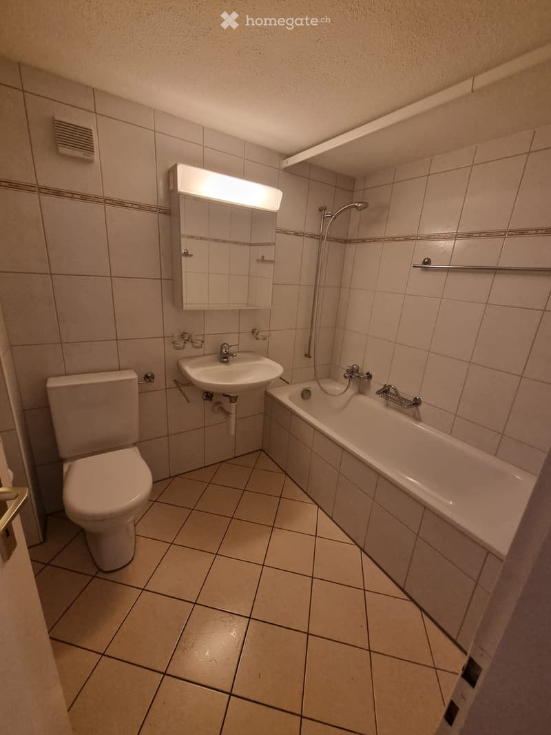 Bathroom with beige tiles, a toilet, a sink, a bathtub, a mirror with built-in lighting, and a showerhead.