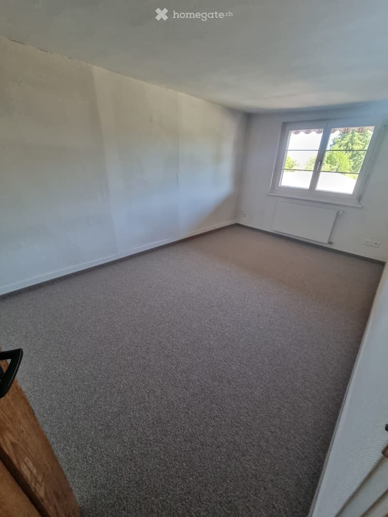 Empty room with light-colored walls, carpeted floor, and a single window with white frame and blinds.