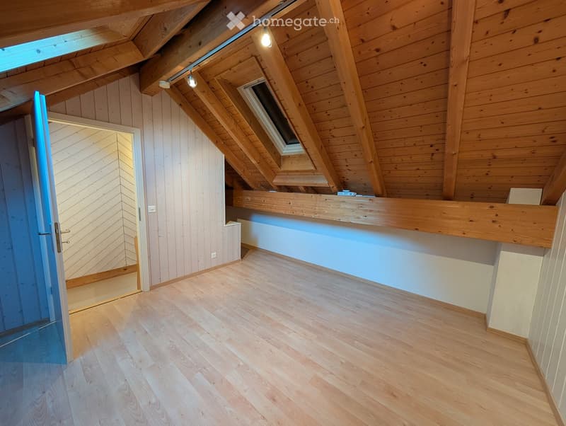 Empty attic room with wooden beams, skylight windows, and light wooden flooring. No furniture or equipment present.
