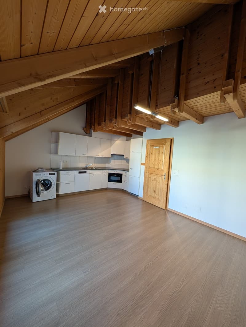 Modern kitchen with white cabinets, a sink, a washing machine, and an oven, featuring wooden beams on the ceiling and light wooden flooring.