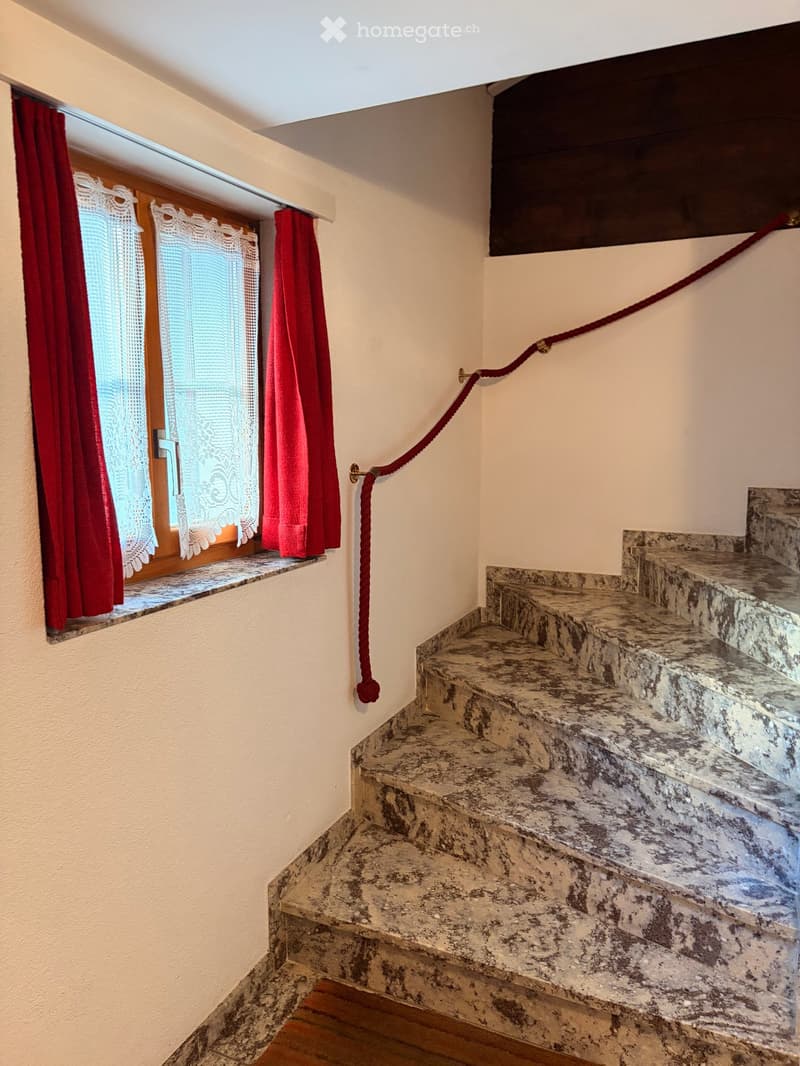 Staircase with marble steps and a red rope handrail, adjacent window with red curtains and lace trim.