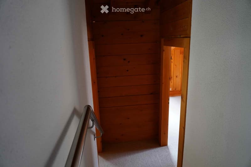 Wooden staircase with metal railing, leading to an open doorway with light-colored walls and wooden trim.