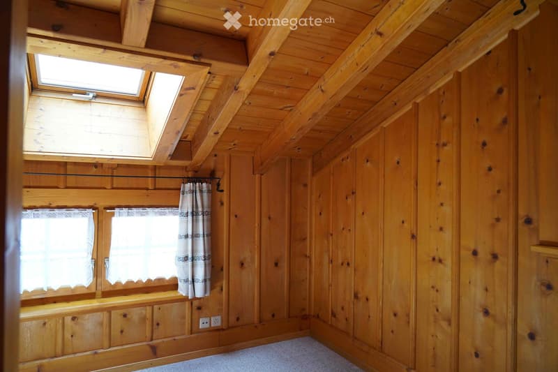 Empty wooden room with exposed beams, skylight, and built-in wooden cabinetry. The room features wooden walls, a carpeted floor, and white curtains on the windows.