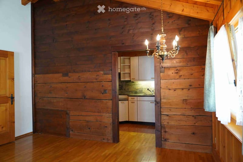 A wooden-paneled room with a chandelier, a small kitchen area with cabinets and a sink, and a wooden door.