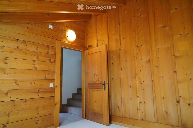 Wooden-paneled hallway with a recessed ceiling light, an open wooden door leading to a carpeted staircase, and visible electrical outlets on the wall.
