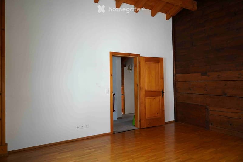 Empty room with wooden flooring, white walls, and wooden doors leading to another space. No furniture or equipment visible.