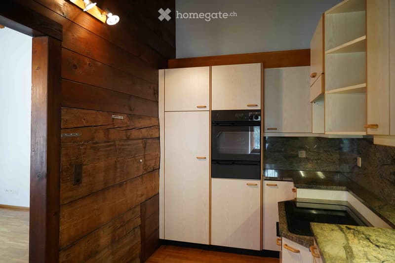 Modern kitchen with white cabinets, wooden accents, granite countertop, and built-in oven.
