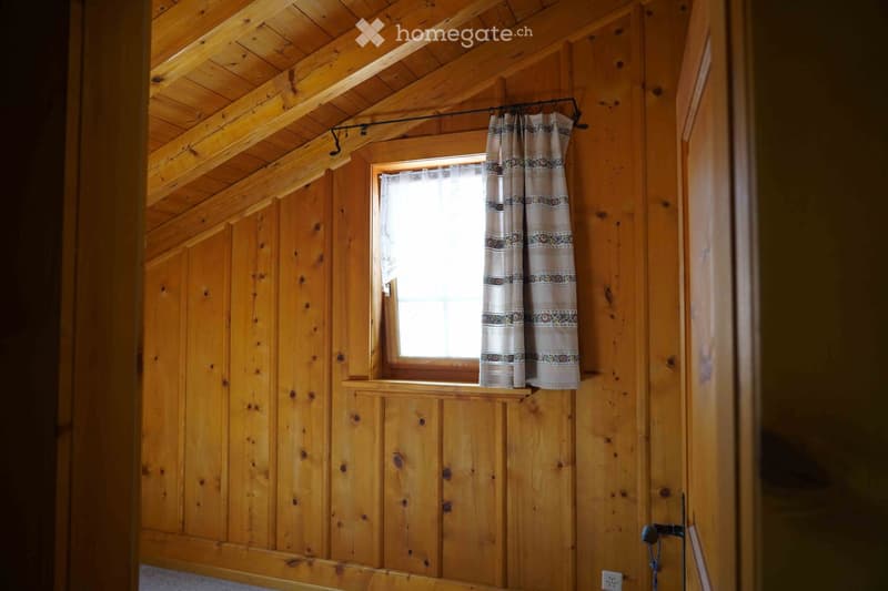Empty wooden room with exposed beams, a window with curtains, and a door.