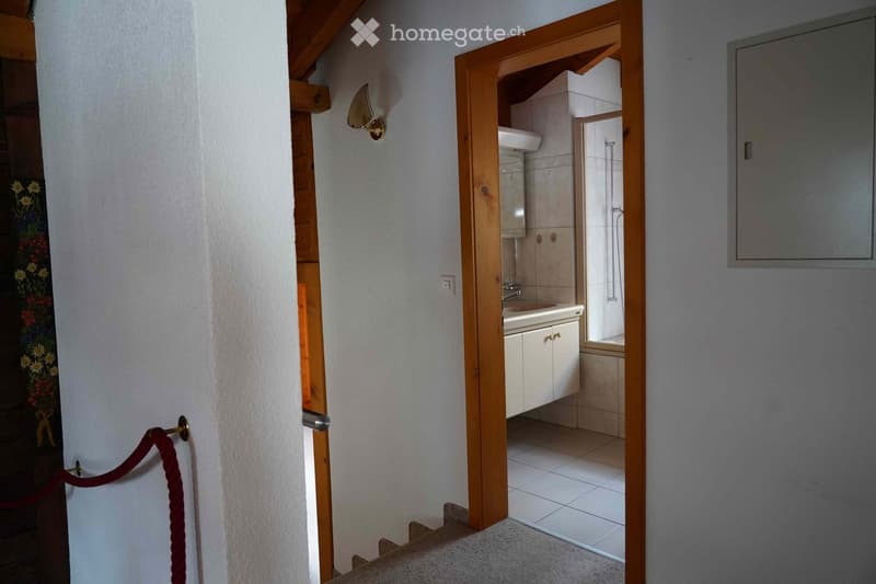 Bathroom with white tiled walls and floor, a white sink with a cabinet below, a shower area, and a wooden door frame.