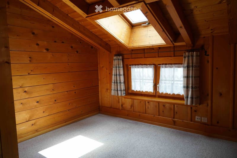 Empty wooden room with exposed beams, skylight, and built-in wooden bench seating along one wall.