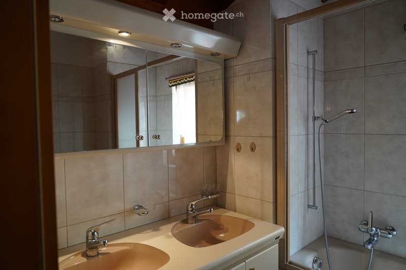 Modern bathroom with two sinks, a large mirror, a shower, and a bathtub. The walls are tiled in beige and grey, and the fixtures are chrome.