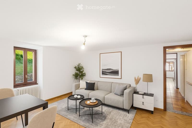 Modern living room with a grey sectional sofa, coffee tables, side tables, chairs, a lamp, a picture frame, and a plant. The room features wooden flooring and large windows with a view of greenery.