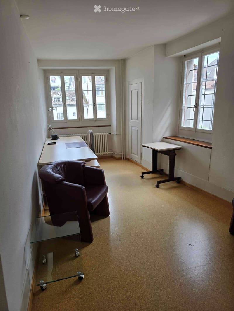 Office space with a brown leather chair, white desk, glass coffee table, and a small table near the window.