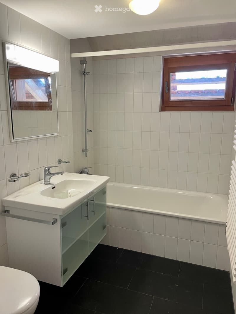 Modern bathroom with white tiles, a double sink, bathtub, mirror, and radiator.