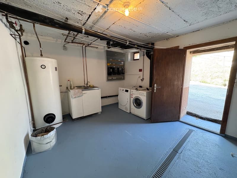 Utility room with a washing machine, water heater, sink, and cabinet, featuring a blue floor and exposed pipes.