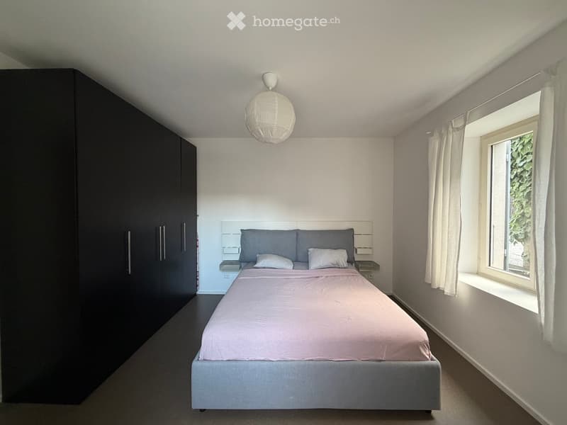 Modern bedroom with a double bed, nightstands, a large wardrobe, and a window with white curtains.