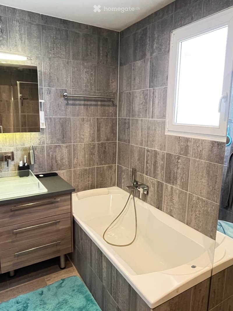 Modern bathroom with a large bathtub, a sink with a wooden cabinet, a mirror, and a towel on the floor.