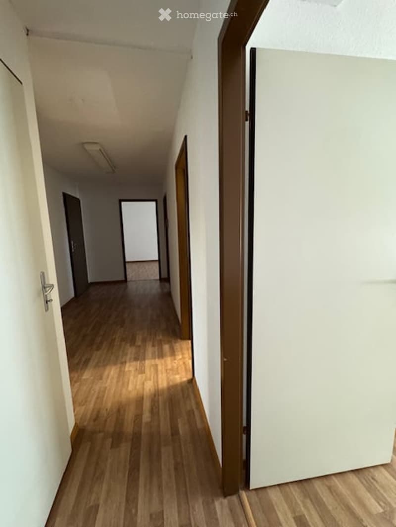 Empty hallway with wooden flooring, white walls, and several doors leading to rooms.