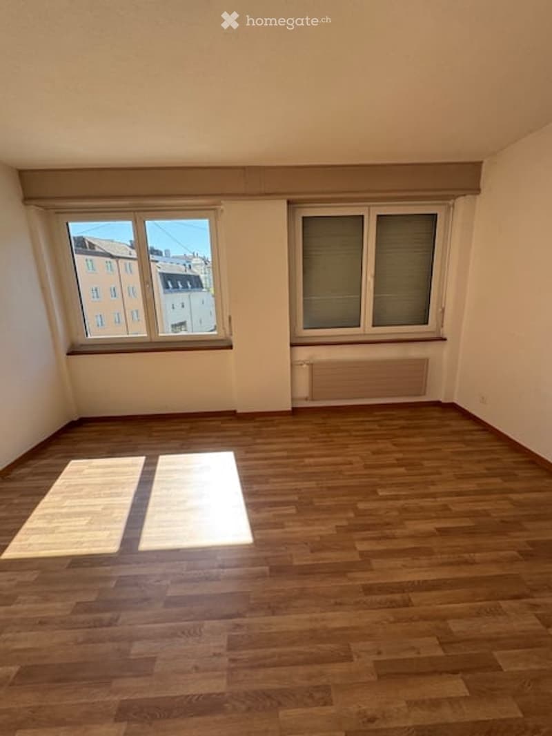 Empty room with wooden flooring, two windows, and natural light streaming in. No furniture or equipment present.