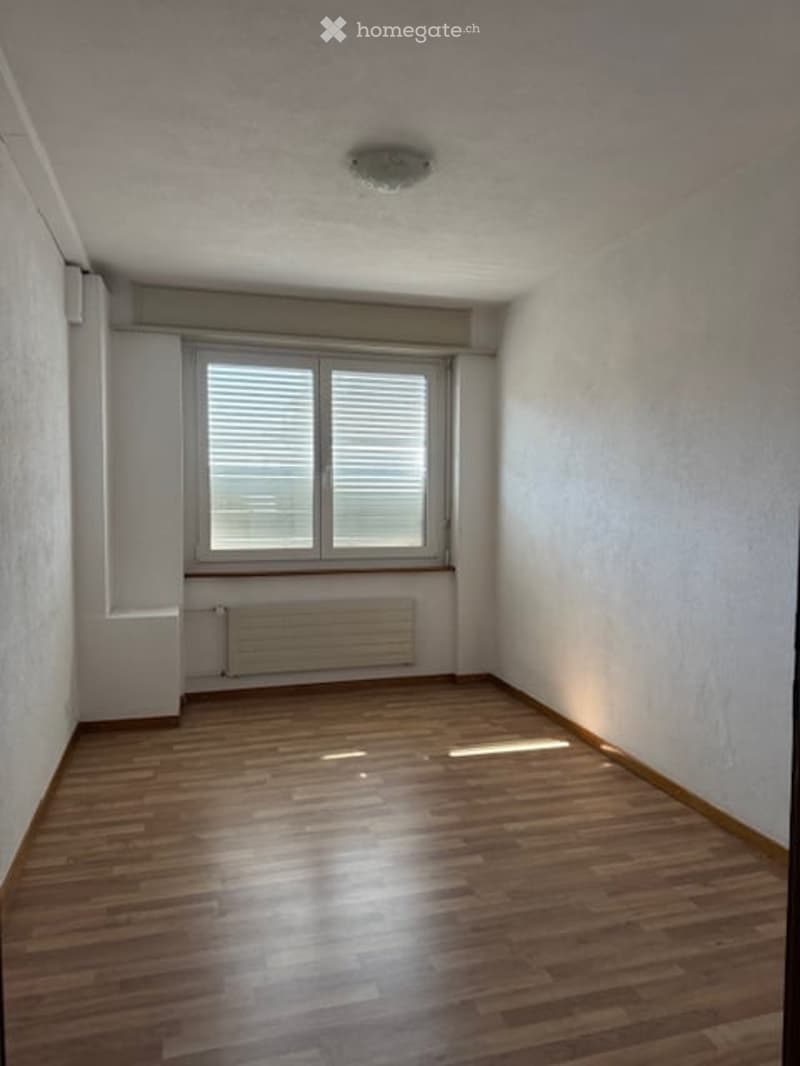 Empty room with wooden flooring, white walls, and a large window with blinds. No furniture or equipment present.