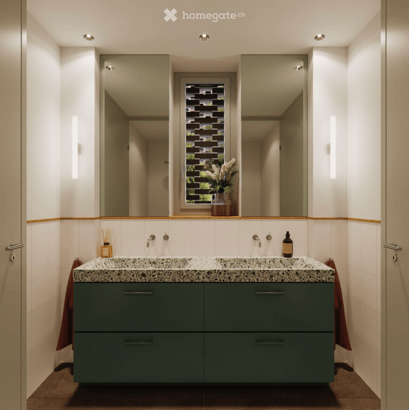 Modern bathroom with a double sink, green cabinetry, marble countertop, and a large mirror. A vase with white flowers sits on the windowsill, and a bottle is placed on the countertop.