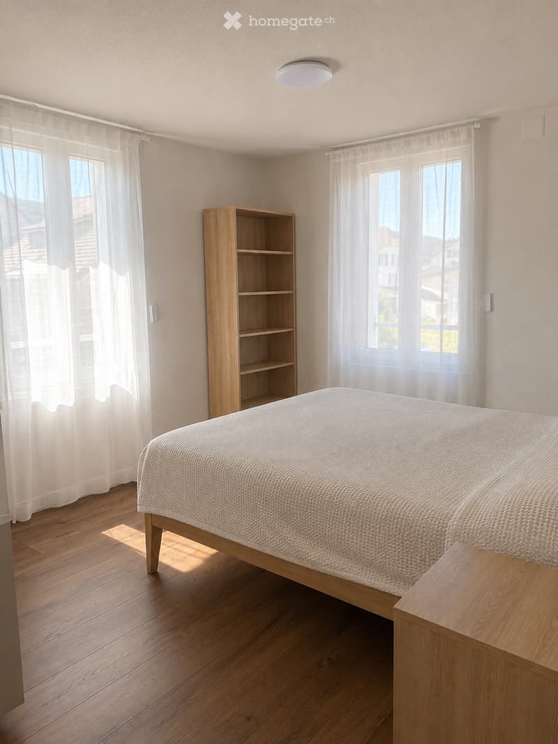 Bright bedroom with wooden flooring, large windows with white curtains, a neatly made bed with a textured duvet, a wooden nightstand, and a wooden shelf unit.