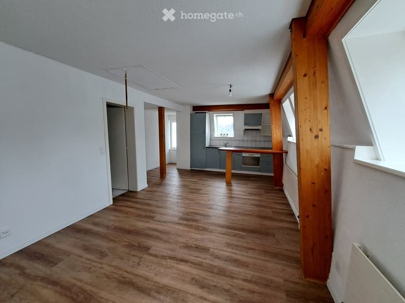 Empty room with wooden flooring, white walls, and visible structural beams. No furniture or equipment present.