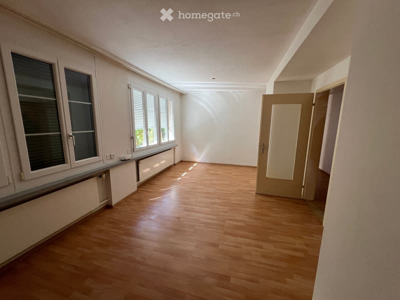 Empty room with wooden flooring, white walls, large windows, and a door leading to another space.