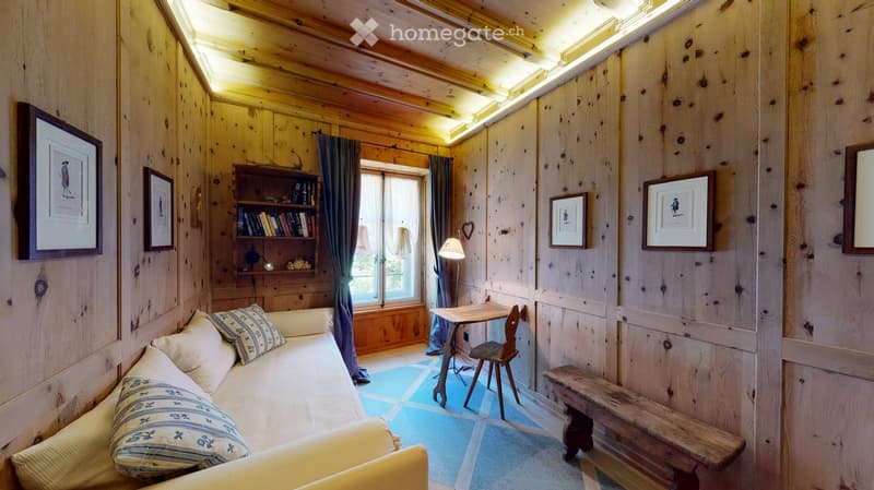 wooden walls, couch with pillows, desk and chair, shelf with books, window with curtain, floor lamp, wooden bench, picture frames
