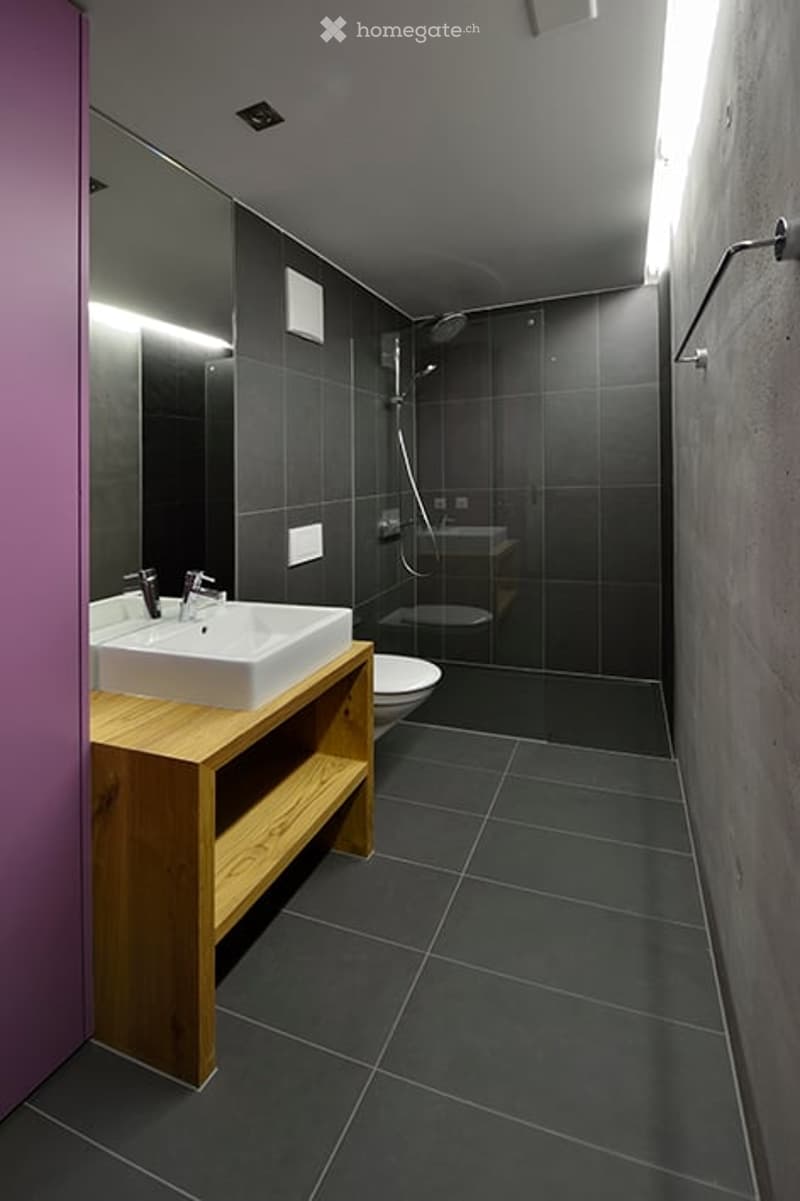 Bathroom with white sink, wooden shelf, shower, toilet, mirror, and gray tiles