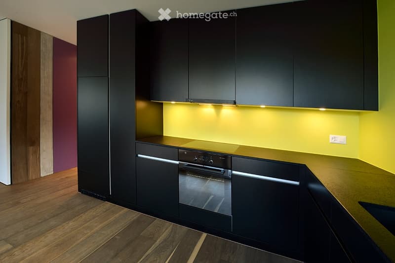 modern kitchen with black cabinets, yellow wall, wooden floor, built-in oven, sink