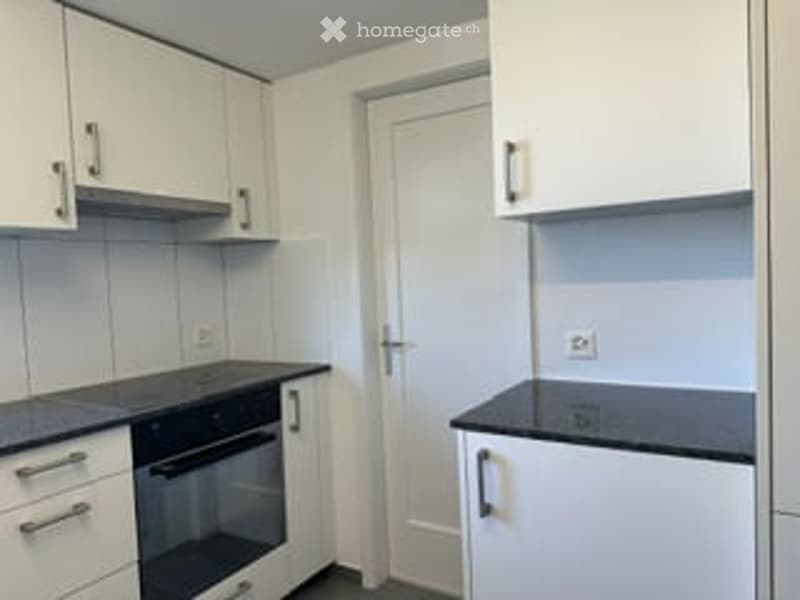Modern kitchen with white cabinets, black countertops, and an integrated oven. The space is clean and well-organized with a door leading to another room.