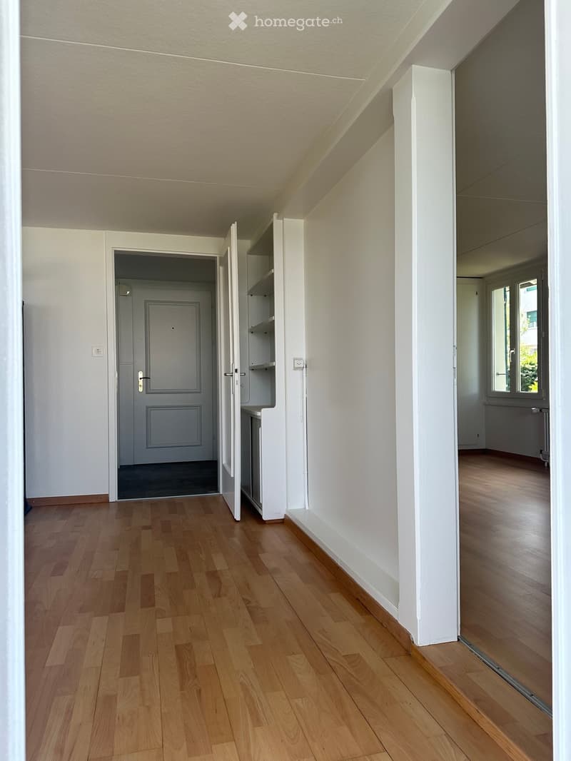 Empty hallway with wooden flooring, white walls, and open doors leading to other rooms.