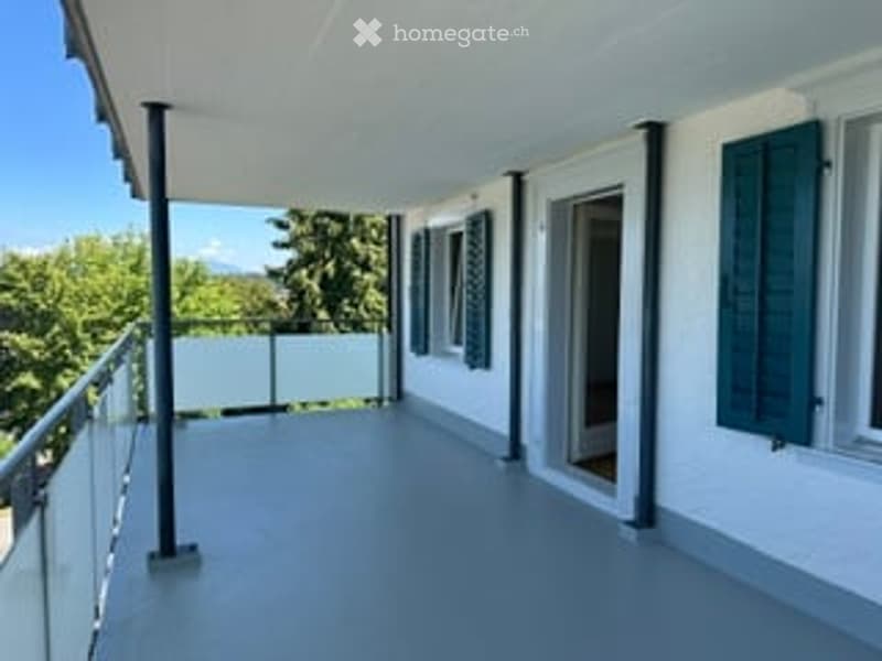 Balcony with white walls, green shutters, glass railing, and a view of greenery.