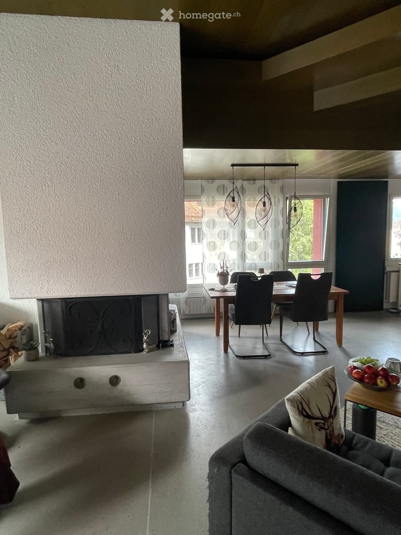 Modern living room with a grey sofa, dining table with chairs, fireplace, and decorative items.