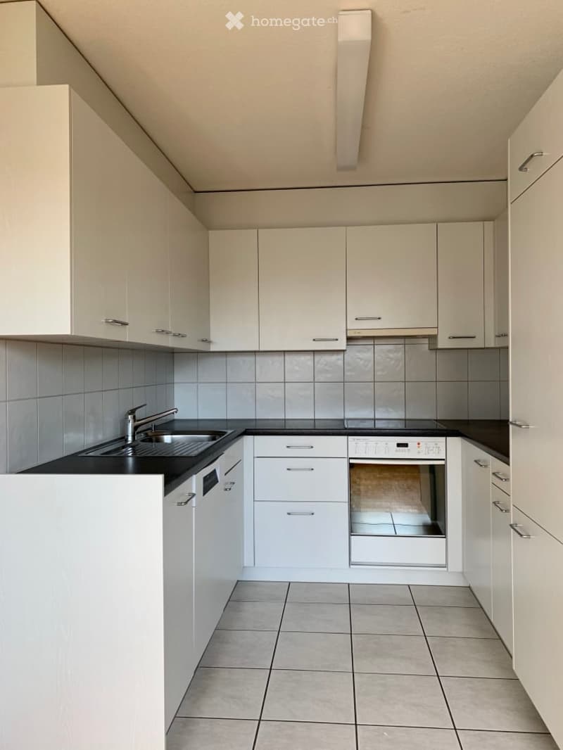 Empty kitchen with white cabinets, black countertops, and tiled flooring. No appliances or furniture are present.