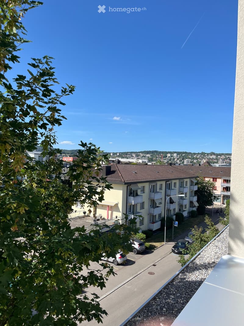 Balcony overlooking a parking lot and multi-story residential building with balconies and awnings.