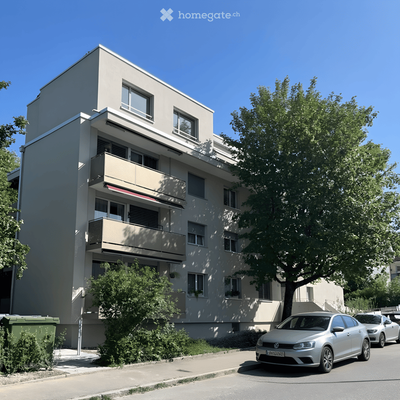 Modern multi-story residential building with balconies, large windows, and a parking area with cars.