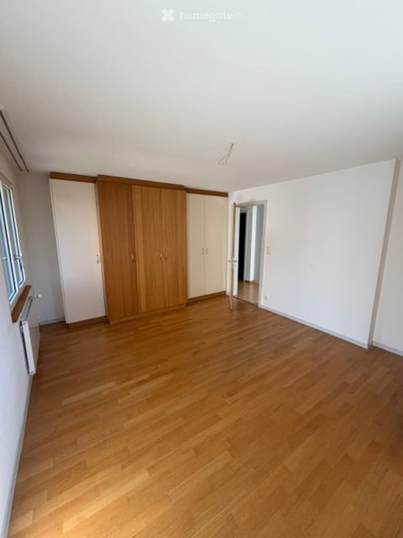 Empty room with wooden flooring, white walls, built-in wardrobes, and a window with blinds.