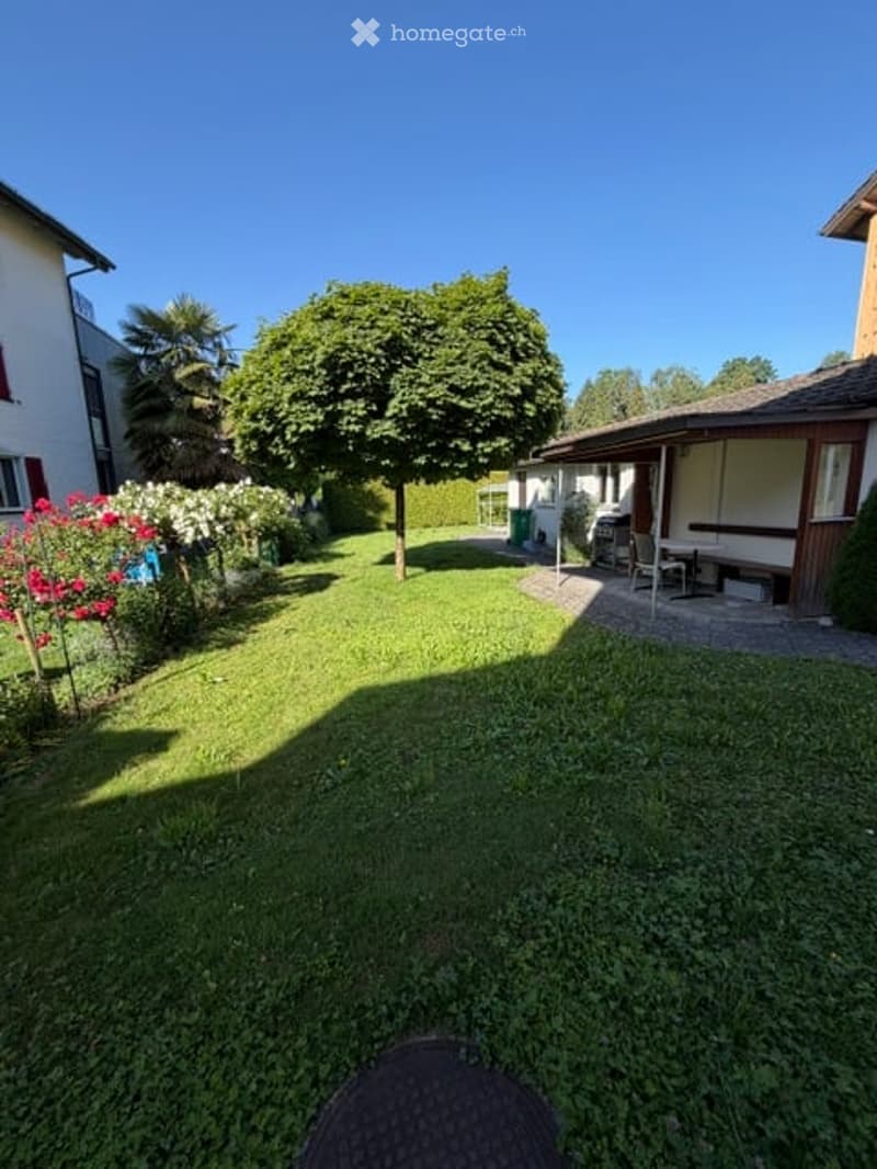 Well-maintained garden with a large tree, flower beds, and a patio area with a table and chairs.