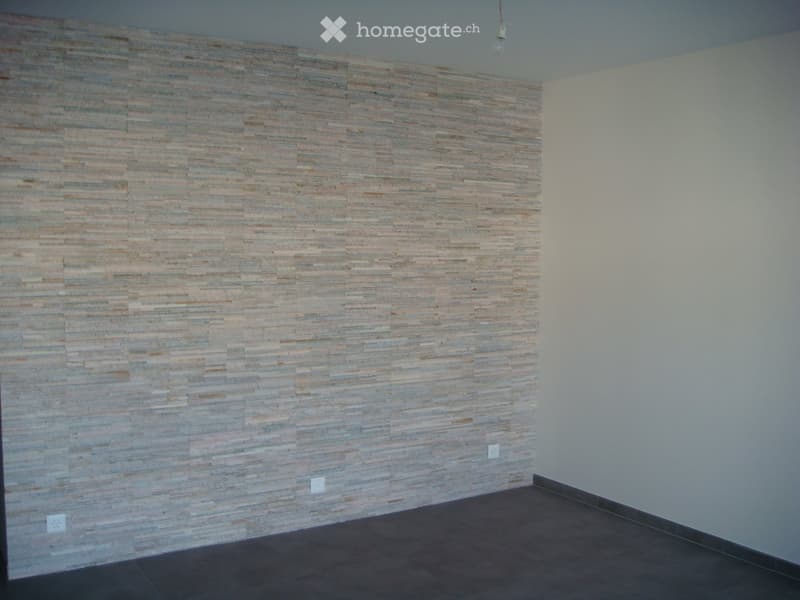 Empty room with a textured, wood-paneled accent wall, white walls, and dark tiled flooring.