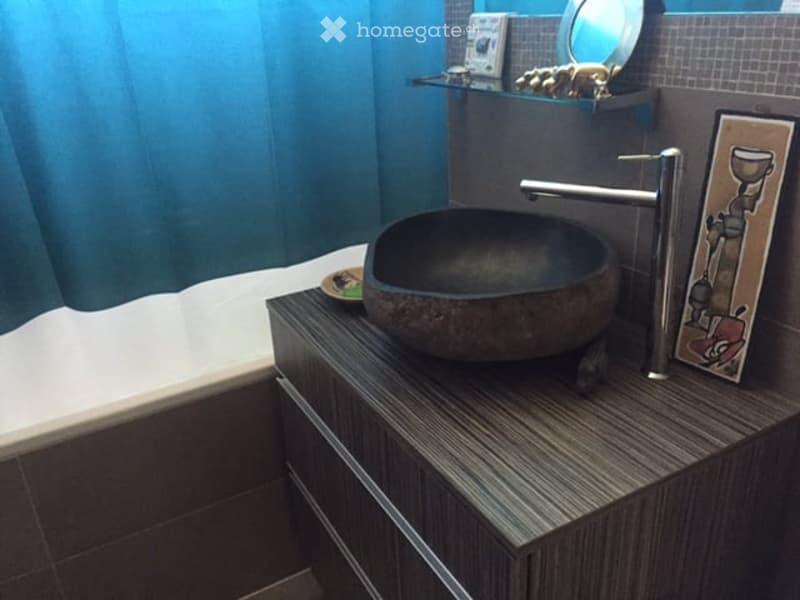 Modern bathroom with a dark, stone sink, sleek faucet, and a glass shelf holding decorative items. Blue curtains and a framed picture add a touch of color.