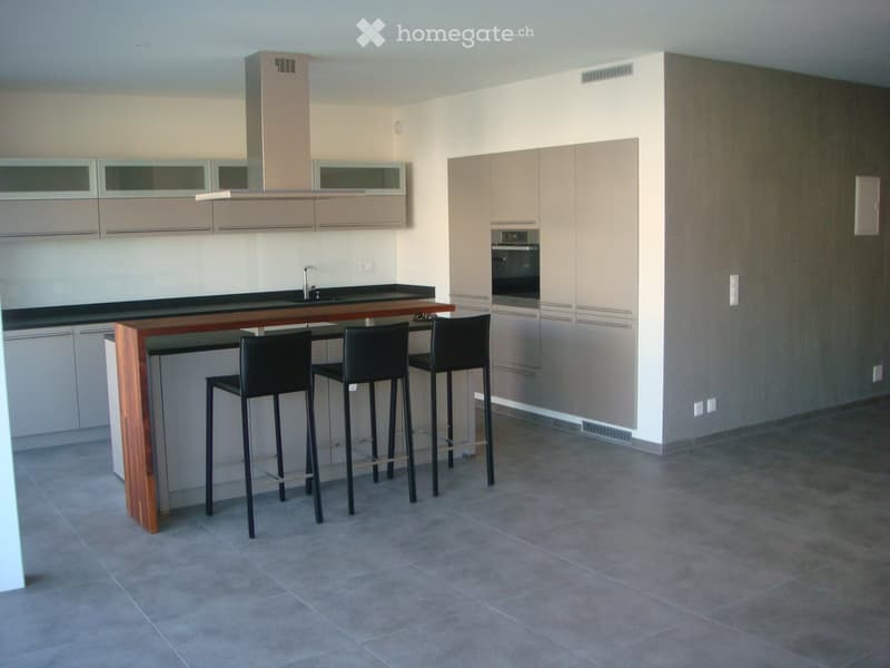 Modern kitchen with light-colored cabinets, a central bar table with two stools, and an integrated oven.