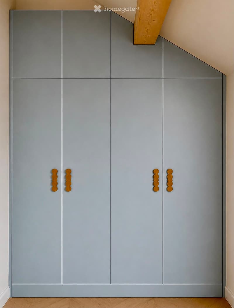 Modern grey built-in wardrobe with wooden handles in a room with light wooden flooring and white walls.