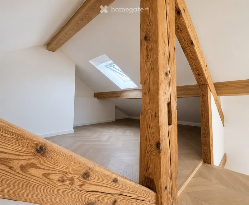 An empty attic space with wooden beams, a skylight window, and wooden flooring.