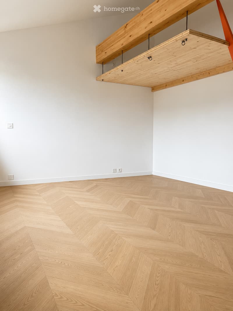 Empty room with light wooden herringbone flooring and white walls, featuring a built-in wooden shelf unit with metal brackets.