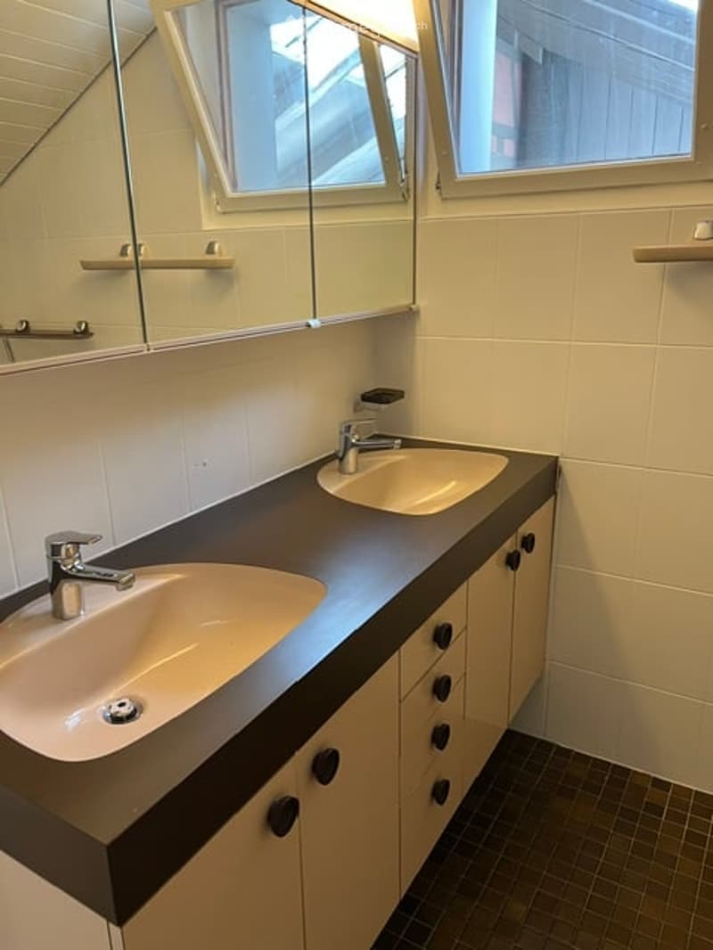 Modern bathroom with double sinks, sleek black countertop, silver faucets, and large mirror above.