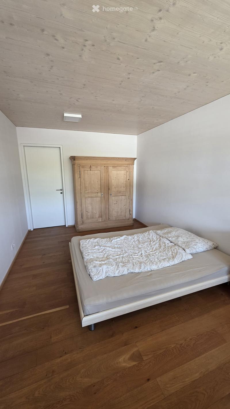 Minimalist bedroom with wooden floor, white walls, a single bed with patterned bedding, and a wooden wardrobe.