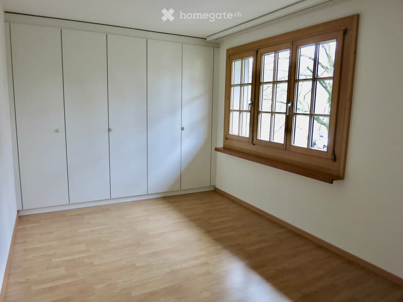 Empty room with light wooden flooring, white built-in wardrobes, and a large wooden-framed window with multiple panes.